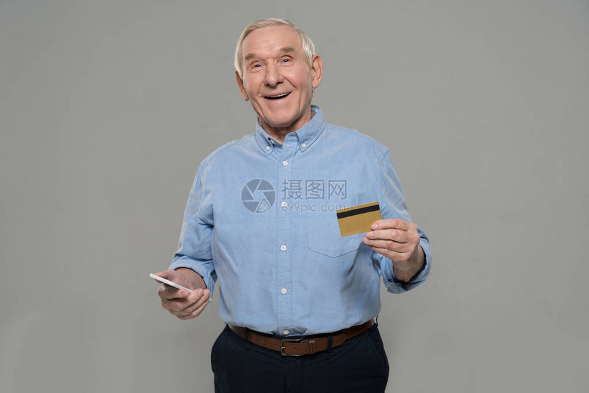 老人持有智能手机和信用卡隔离在灰色背景隔图片