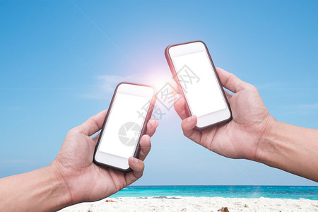 手拿着智能手机在海滩和蓝天背景图片