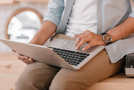 坐在木制桌子上时使用笔记本电脑的青年男子近背景图片