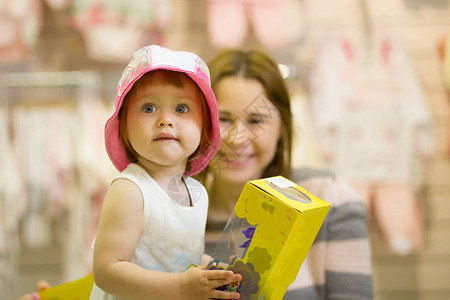 快乐的年轻母亲和戴着帽子的女儿在店里玩图片