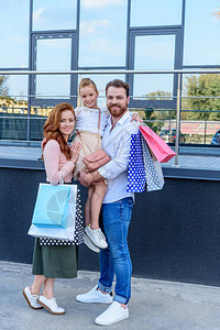 父母和女儿购物后提着购物袋站在街上背景图片