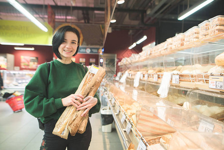 超市里微笑的买家超市手中拿着面包的积极女孩女孩图片