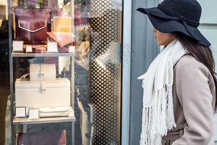 漂亮的年轻女子戴着帽子看着商店橱窗图片