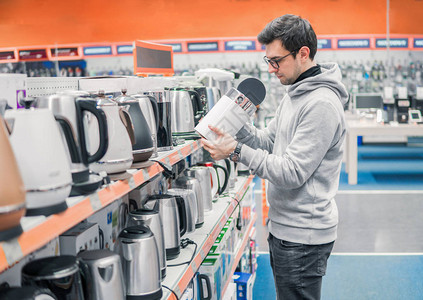 聪明的年轻客户在超市商场国内电子部门选择一个水壶图片