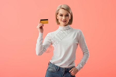 快乐的金发年轻女子拿着信用卡手站在口袋里孤背景图片
