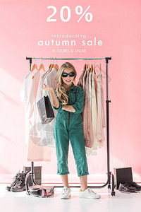穿着时装和墨镜的时髦儿童站在商店服装和鞋铺边购物袋旁边背景图片