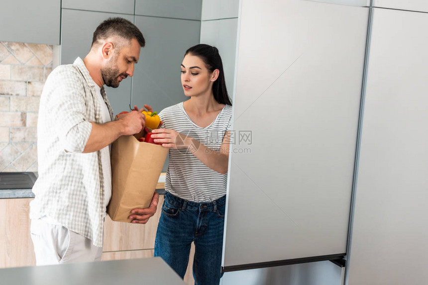 已婚夫妇在家中厨房冰箱里放新鲜蔬菜图片