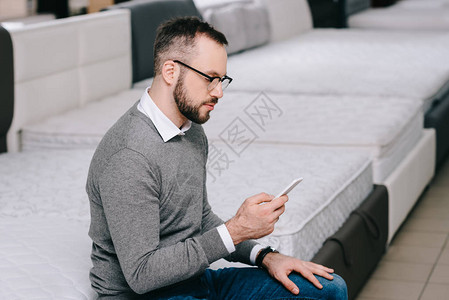 坐在家具店铺床垫上的智能手机的男背景图片