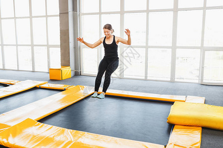 青年女子业余爱好杂技运动员在室内蹦床现代兴趣爱好和健身概念图片