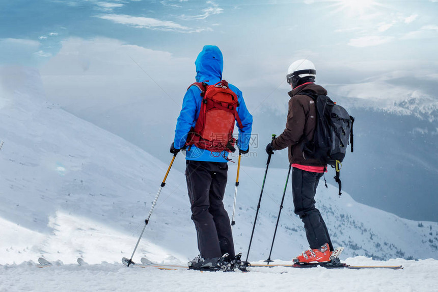 穿着滑雪服的人们正坐在山顶的雪地上图片