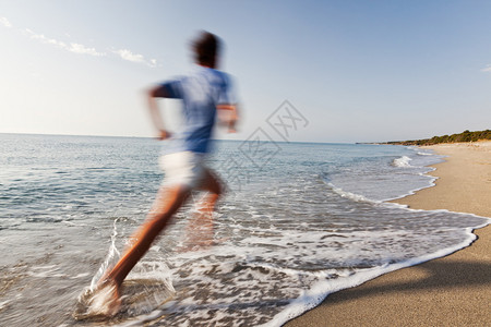 赤脚裸足在荒漠热带海滩的海洋边界上跑动的Athletic图片