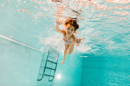可爱的孩子在游泳池的蓝色水中游泳图片