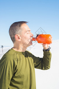 成年运动男子在冬季在雪坡上登山时喝酒保持水分的重要概念阳光明媚的日子图片