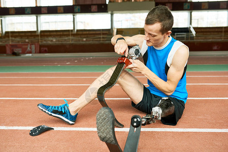 坐在现代健身修补假肢脚地板上的年轻截肢运动员图片