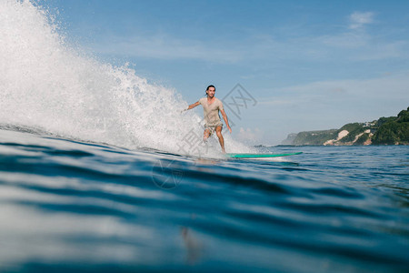 身穿湿T恤的青年男子在度假时在冲浪板上骑图片