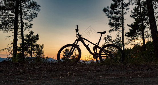 山地自行车日落剪影在森林小径上图片