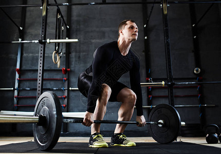 肌肉男运动员在健身房锻炼时用力从地板上举起重图片