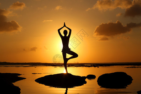 日落时在海边练习瑜伽的女人剪影图片