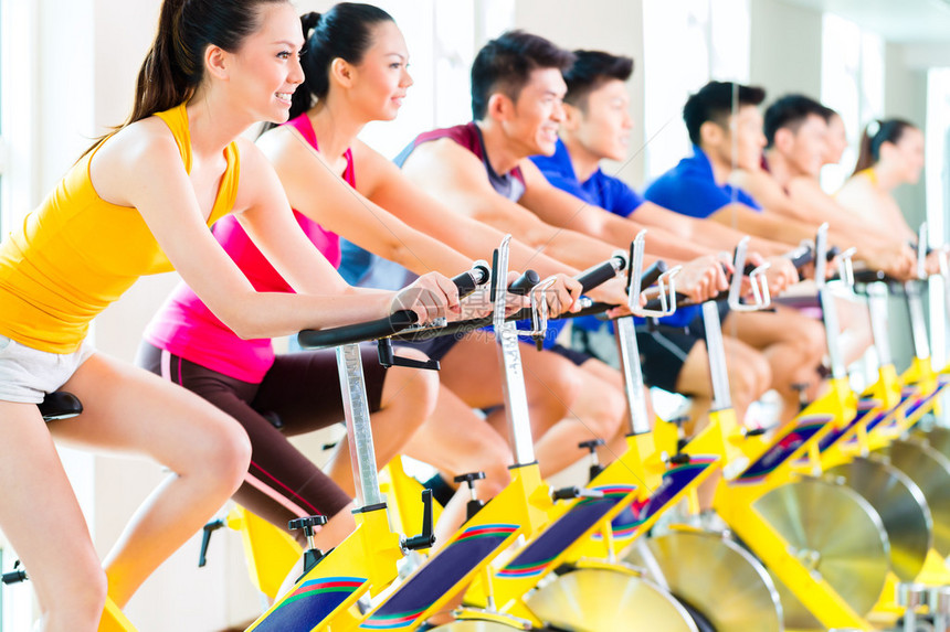 参加健身俱乐部或运动会的亚洲运动组男女在旋转自行车图片