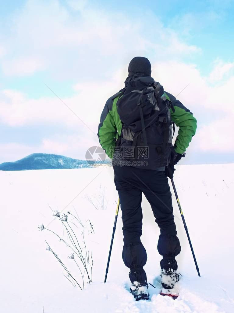 有雪鞋和背包的人在雪地里休息穿着冬季夹克和徒步裤在粉雪中穿雪鞋行走的徒步旅行者多云的冬日图片