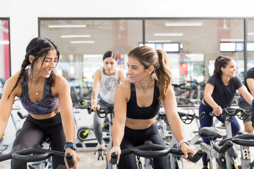 女客户在健康俱乐部中一边微笑一边骑脚踏自行车图片