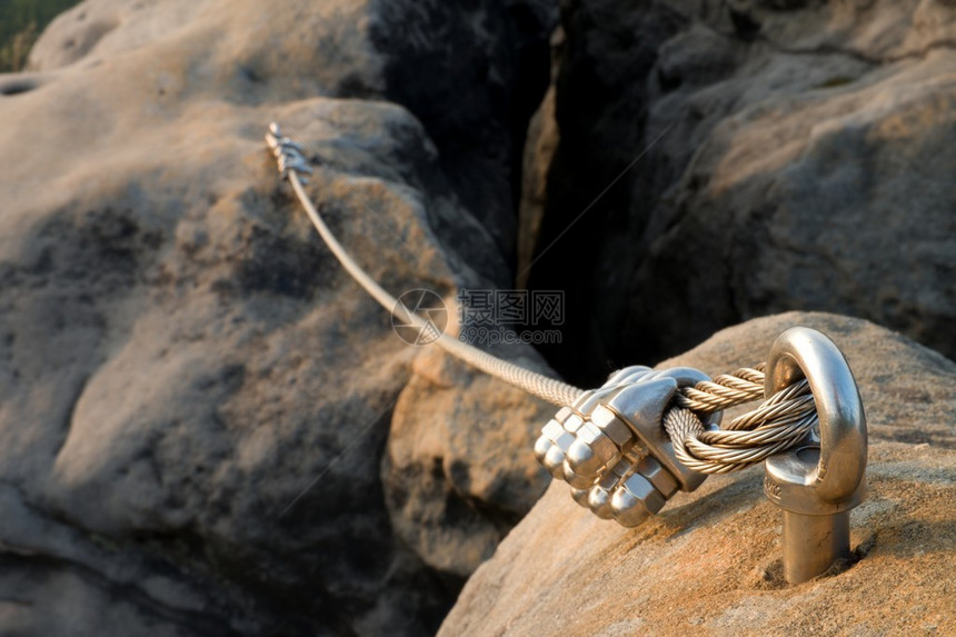 铁绞绳在登山者补丁的岩石之间伸展绳索通过螺钉卡钩固定在块中锚定在砂岩石图片