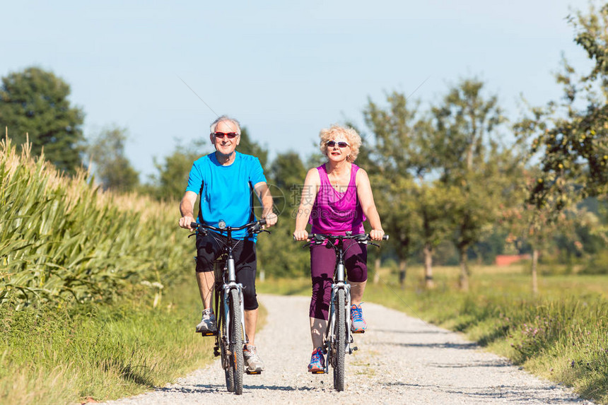 一对活跃的老年夫妇在夏日阳光明媚的乡村骑自行车时享受退休生活图片