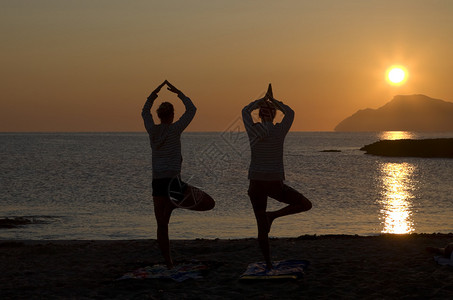 两名妇女在黎明练习瑜伽的剪影图片