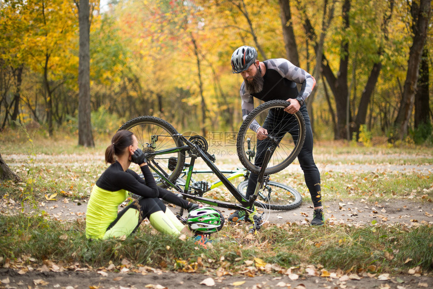 成人男子修自行车而其女友则坐在草地上和图片