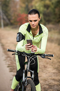 坐在自行车上在公园使用智能手机的年轻女骑图片