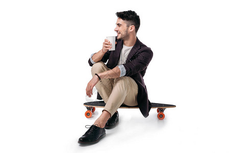 年轻男子在坐滑板上喝彩杯里的饮料背景图片
