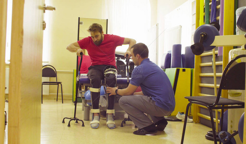 医生理疗师在康复诊所将矫形术放在残疾青年男子的腿图片
