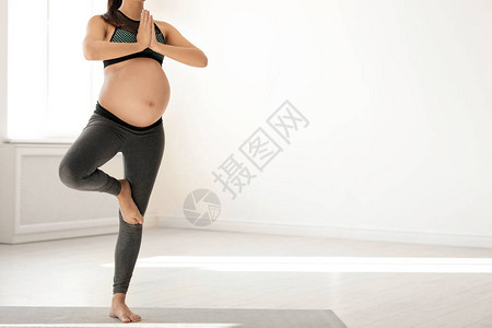 身着健身服的年轻孕妇在家里做瑜伽图片