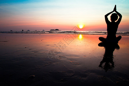 日落时在海滩上冥想的女人的剪影图片