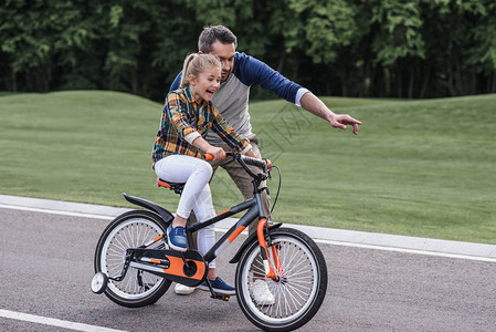 年青父亲在沥青路上教女儿骑自行车图片