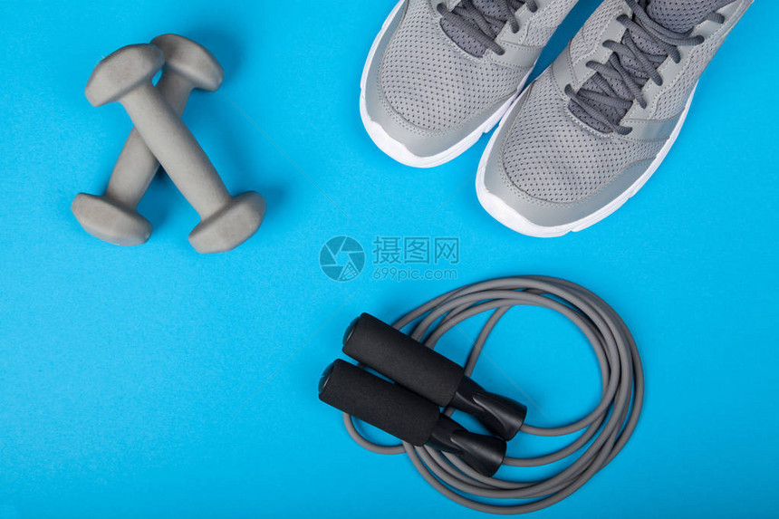 蓝色背景上的运动鞋哑铃和跳绳顶视图健身运动和健康的图片