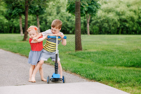 两个小高加索学龄前儿童互相打架男孩和女孩不能共用一辆滑板车哥不把玩具给妹背景图片
