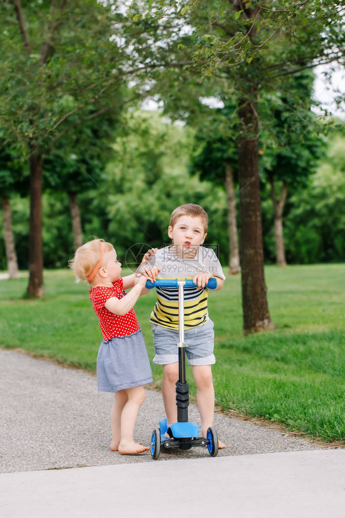 两个白种人学龄前儿童在外面的公园里打架男孩和女孩不能共用一辆滑板车哥不把玩具给妹图片