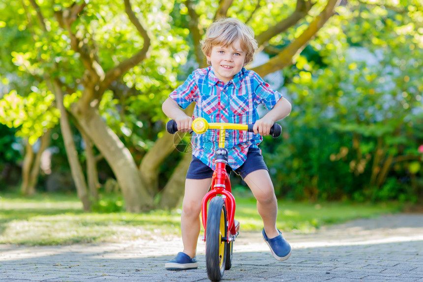 快乐的金发男孩穿着五颜六色的衣服在国内花园里驾驶自行车蹒跚学步的孩子在温暖的夏日做梦和玩乐户外图片