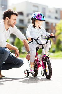 小女孩跟爸一起学骑自行车的小女背景图片