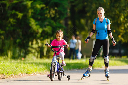 年轻母亲在公园骑自行车与女儿图片