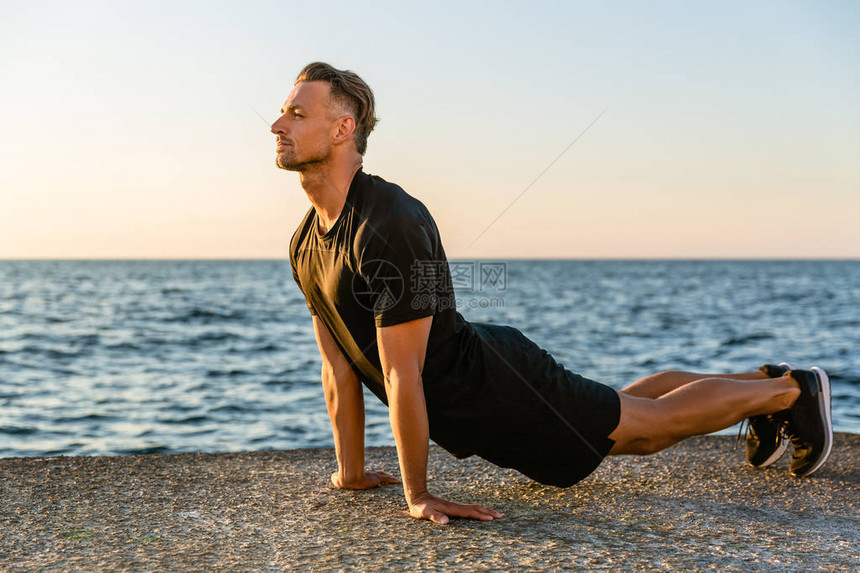 英俊的成人运动员在海边伸展图片