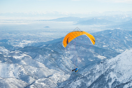 滑翔机以明亮的橙色风筝飞越山上图片