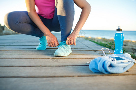 跑鞋系鞋带的女人夏末或秋季女运动健身跑步者准备在海滨户图片