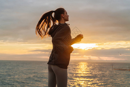 长头发的运动长发女孩在日落时去海边跑图片