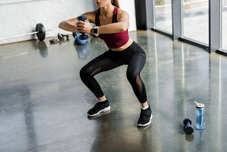 运动女运动员在健身中心用哑铃进行蹲下锻炼时的图片