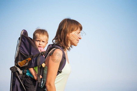 一个男孩坐在背包里孩子和他的父母一起旅行带着孩子爬山妈带着孩子一个小旅人一个女人带着她的孩子背景图片