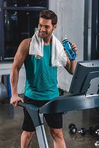 在健身房的跑步机上用毛巾和运动瓶训练微笑图片