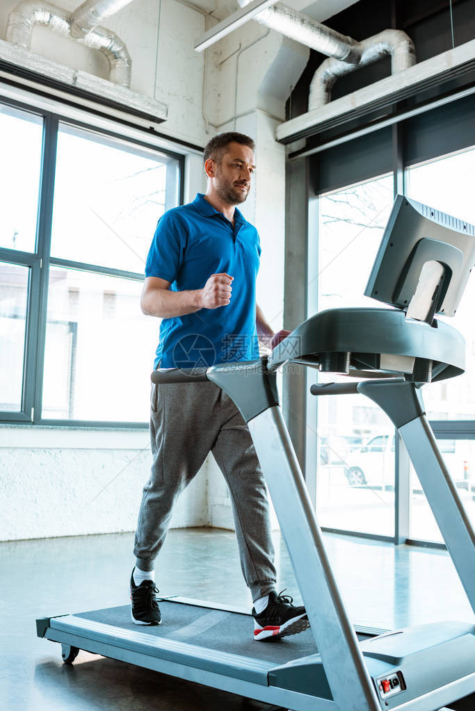 英俊的男人在健身房的跑步机上跑步图片