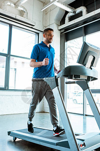 英俊的男人在健身房的跑步机上跑步图片